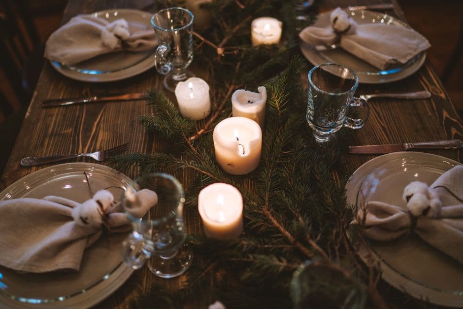 Warm and elegant Christmas table with candles, glassware, and pine decor for festive dining.