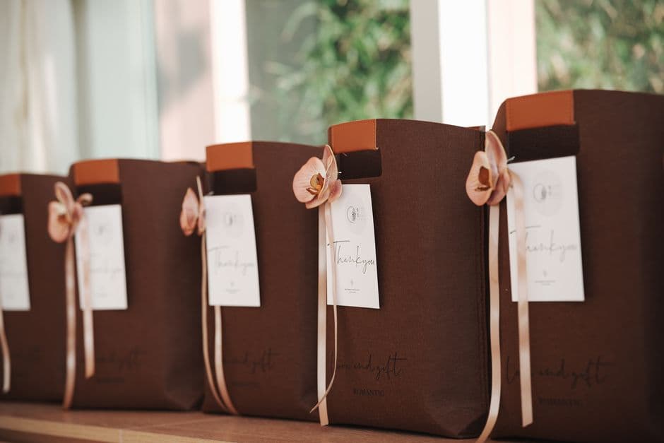 A row of elegant brown gift bags adorned with pink flowers and thank you notes, perfect for events.
