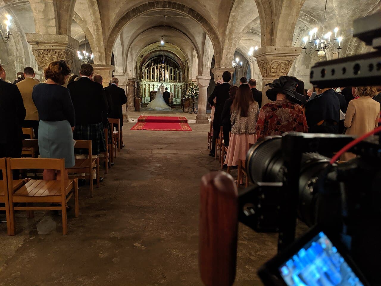 Video camera in the foreground recording a wedding ceremony in a church crypt